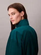 Campera tipo track Calvin Klein de tejido plano en color verde oscuro, de corte cropped y manga larga. Cuenta con cuello alto, cierre frontal de cremallera metálica, bolsillos laterales y elástico acanalado a rayas en los puños y el dobladillo. Presenta el logo de la marca bordado en el pecho.