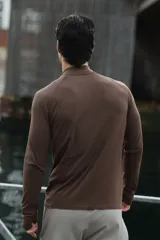 Remera deportiva marrón con cuello alto, cierre frontal parcial y mangas largas raglán, confeccionada en tejido técnico con paneles texturizados y corte ajustado.