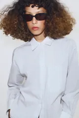 Camisa de algodón con estampado de rayas verticales, cuello solapa y puños en color blanco a contraste. Presenta cierre frontal con botones, bolsillo de plastrón en el delantero y bajo asimétrico.