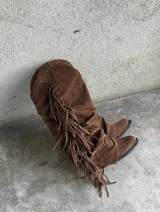 Botas altas de gamuza marrón con diseño slouchy, punta fina y flecos largos colgantes en los laterales.