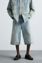 Bermudas de denim de algodón, color celeste claro con efecto lavado y manchas marrones/beige en las perneras. Tienen un corte ancho (baggy fit) y terminación de bajo irregular.