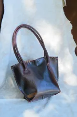 Cartera de cuero con textura crocco y silueta estructurada, manijas largas, detalles de terminación artesanal en los bordes y clip de cierre.