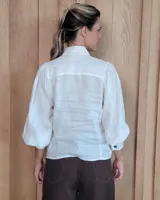 Camisa de lino color blanco con cuello camisero clásico, cierre frontal de botones y mangas largas abullonadas con puños anchos.