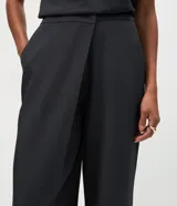 Pantalón de sastrería color gris oscuro, de tiro alto y corte recto. Presenta un diseño sofisticado con un cruce frontal superpuesto en la cintura y cierre oculto.