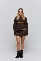 Sweater de punto marrón de tejido liviano y calce relajado, con hombros caídos, cuello redondo y puños y cintura en rib. Cuenta con una estampa tejida en el frente con la frase "Estoy Blessed" en color amarillo.