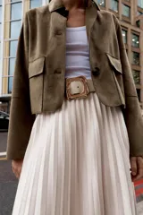 Falda midi plisada de tiro alto color beige, con cinturón a tono y hebilla metálica dorada. Cierre lateral con cremallera oculta.