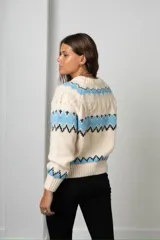 Buzo tejido de punto con diseño de guardas geométricas en tonos celeste y negro sobre base color crema. Presenta cuello redondo, mangas largas y puños acanalados.
