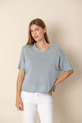 Sweater de punto de manga corta en color celeste, con cuello redondo y detalle de abertura frontal. Presenta un corte holgado y diseño minimalista.