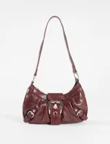 Cartera de hombro color bordó, confeccionada en cuero sintético con acabado brillante. Presenta un diseño estructurado con frunces laterales, una hebilla metálica central decorativa y dos correas laterales con hebillas pequeñas. Incluye una correa de hombro fija y cierre superior.