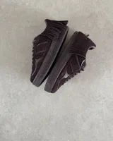 Zapatillas bajas de cuero vacuno color marrón chocolate, con cordones y detalle de flecos en el tobillo.