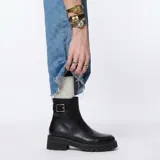 Bota de cuero negro de caña media con suela track dentada y detalle de tira con hebilla metálica en el tobillo.