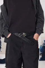 Cinturón de cuero negro con perforaciones decorativas a lo largo de toda la tira y hebilla metálica ovalada con detalle central.