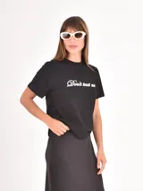 Remera negra de algodón con cuello redondo y mangas cortas, presenta la frase 'Don't text me' estampada en el centro del pecho con tipografía cursiva blanca.
