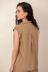 Conjunto compuesto por una blusa sin mangas con cuello camisero, bolsillos frontales y cierre de botones, y un pantalón largo de corte recto y holgado, ambos confeccionados en tejido texturizado de color marrón.