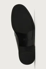 Mocasín de vestir color marrón oscuro, confeccionado en cuero, con detalle de antifaz y borlas decorativas en el empeine. Presenta una horma redonda y suela plana a tono.
