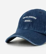 Gorra de sarga de algodón color azul denim, con visera curva y cierre ajustable con hebilla. Presenta bordado en blanco en la parte frontal con el texto "RIO DE JANEIRO BRASIL".