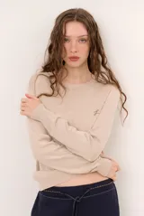 Sweater de punto color beige, de cuello redondo y manga larga, con detalle de pequeño bordado en el pecho.