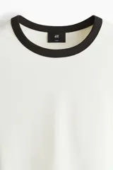 Remera de algodón en color blanco con cuello y bordes de mangas en contraste color negro. Presenta un diseño de corte holgado con hombros caídos y bajo recto.