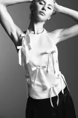 Top blanco de cuello halter y hombros descubiertos, con detalle de lazos en el delantero y cierre en la espalda con tira ajustable.