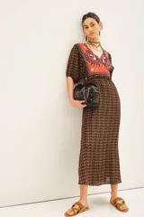 Vestido largo de viscosa con estampado geométrico en tonos marrones y detalle de bordado colorido en el escote en V. Presenta mangas cortas con frunces y puños elásticos, cintura elástica y cierre lateral invisible.
