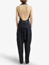 Enterito negro de lana virgen con escote halter profundo y pantalón de inspiración sarouel con cierres metálicos frontales regulables. Incluye cinto fino de cuero negro con hebilla metálica.