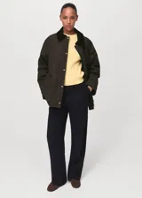 Parka verde militar con cuello camisero de pana negra, cierre frontal de cremallera y botones a presión, bolsillos frontales con solapa y forro interior.