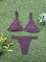 Conjunto de bikini color bordó de tejido fruncido, compuesto por un corpiño de triángulo fijo con tirantes anchos y una bombacha colaless regulable con argollas doradas en los laterales.