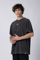 Remera de corte holgado con efecto de lavado ácido en tono gris oscuro. Presenta un pequeño estampado gráfico en el centro del pecho con la inscripción 'ASTRAL ENERGY' y las siglas 'VCP'.