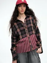 Camisa de corte relajado con diseño combinado. La parte superior presenta un estampado a cuadros en tonos marrones y negros, mientras que la parte inferior destaca por un panel de rayas verticales en color bordó. Cuenta con cierre frontal de botones y mangas largas.