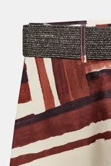 Falda midi de tiro alto en tejido de popelín con diseño evasé. Presenta un estampado geométrico en tonos tierra, crema y negro, e incluye un cinturón a juego con hebilla metálica dorada. Cuenta con cierre lateral mediante cremallera oculta.