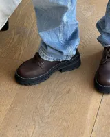 Borcego de cuero color gris con cordones color naranja, suela track negra de goma y detalle de gamuza en la parte superior del tobillo.