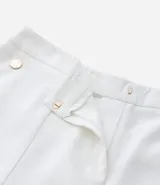Bermuda de crepé color blanco, de corte holgado y tiro alto, con pliegues frontales y bolsillos laterales con detalle de botones. Confeccionada en poliéster y elastano.