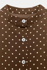 Top entallado de popelín color marrón con estampado de lunares blancos. Presenta cuello redondo, cierre frontal con botones y bolsillos de plastrón en la parte delantera.