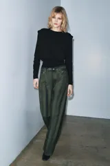 Jersey de punto negro con cuello redondo, manga larga y hombreras marcadas con pliegues.