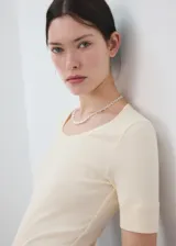 Camiseta de punto de algodón en color beige claro, con cuello redondo y mangas cortas. Diseño ajustado y estilo minimalista.