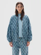 Campera bomber de denim con estampado de cuadros tipo argyle en tonos de azul. Presenta cierre metálico frontal, bolsillos delanteros con solapa y botón, y un ajuste oversized.