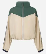 Campera rompeviento de diseño tricolor con bloques de color en verde, beige y blanco. Presenta cuello alto, cierre frontal con cremallera, mangas raglán y puños ajustados. El ruedo incluye un cordón regulable para un ajuste personalizado.
