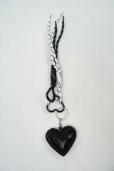 Llavero decorativo con tiras de cordón trenzado en blanco y negro, mosquetón en forma de corazón y un dije acolchado en forma de corazón con textura símil serpiente de color negro.