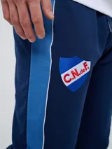 Pantalón de jogging azul marino Umbro del Club Nacional de Football, con cordón ajustable en la cintura, puños elastizados en los tobillos y bandas laterales en tonos de azul. Cuenta con el escudo del club en una pierna y el logo de la marca en la otra.