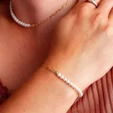 Pulsera de cadena dorada con eslabones y perlas blancas.