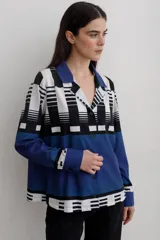 Camisa de manga larga con cuello solapa y cierre frontal de botones. Presenta un diseño estampado con bloques geométricos en tonos azul, blanco y negro.