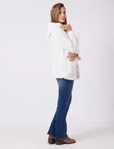 Campera tipo teddy de textura suave y esponjosa en color blanco, con cierre frontal mediante botones y detalles de apliques en cuero sintético negro en la solapa. Presenta bolsillos frontales y un diseño cómodo y abrigado.
