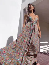 Vestido largo de estilo boho, con estampado tipo paisley en tonos tierra, turquesa y rosa. Presenta un escote profundo con tirantes finos y detalles de bordados florales en color rojo y verde a lo largo del frente.