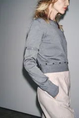 Jersey de punto de cuello redondo y manga larga, con diseño cropped. Presenta detalles de costuras con botones que permiten desmontar partes de la prenda en las mangas y en la cintura.