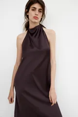 Vestido largo de satén negro con cuello halter y escote fluido. Presenta cierre con cremallera oculta en la espalda y lazada en el cuello.