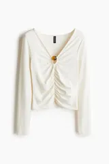 Top corto de punto elástico color blanco, con escote en V, mangas largas y una sección cut-out con una cuenta decorativa en tono ámbar. Presenta costuras fruncidas en la parte delantera para un efecto drapeado y un corte ceñido.