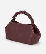 Bolso de mano pequeño color borgoña, con cuerpo de forma trapezoidal y asas cortas trenzadas. El material parece ser cuero sintético (PU).