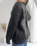 Sweater negro de punto con cuello redondo y mangas largas. Presenta detalles de flecos en forma de rombos en la parte delantera y en las mangas.