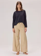 Pantalon de corte ancho y holgado, color beige, con costuras decorativas verticales a lo largo de las piernas. Presenta cintura con botón y cierre frontal.