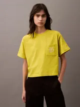 Remera corta color amarillo con cuello redondo, mangas cortas y bolsillo en el pecho con escudo bordado en blanco.